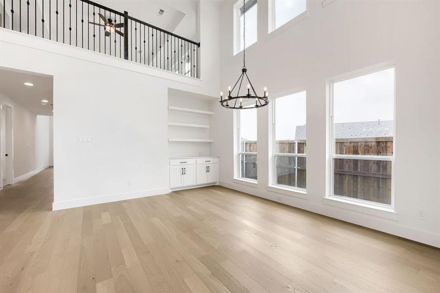 Spacious room featuring soaring ceilings, abundant natural light from multiple windows, wood-finish flooring, built-in shelving, and a decorative chandelier