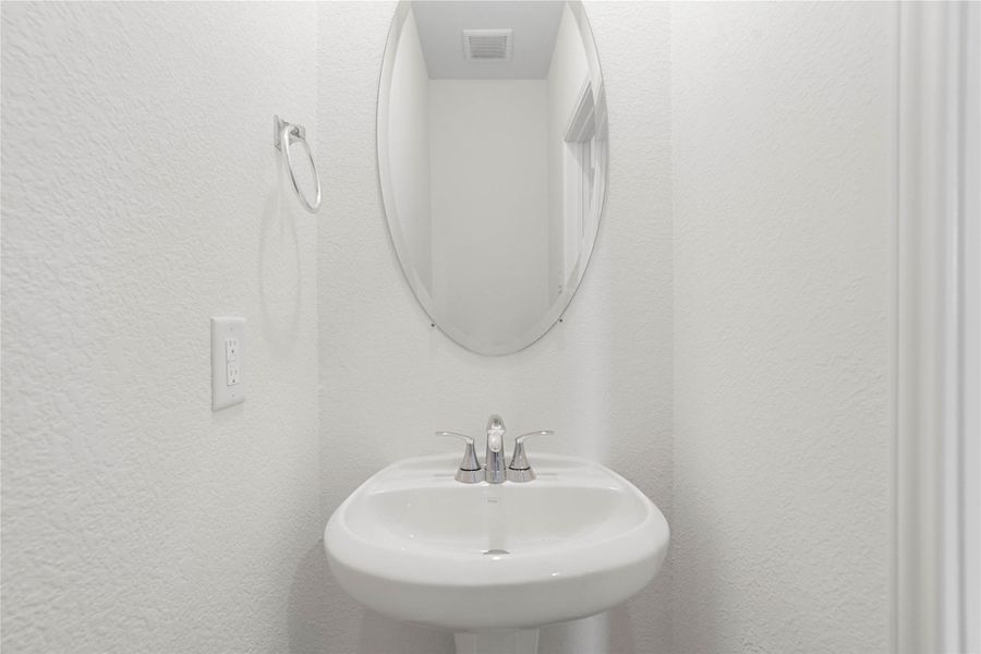 The powder room on the first floor includes a pedestal sink, mirror, and toilet to conveniently meet your needs.