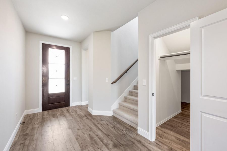 Entryway with dark wood front door, wood-look floors, carpeted staircase, and open closet doorway Entryway with dark wood front door, wood-look floors, carpeted staircase, and open closet doorway