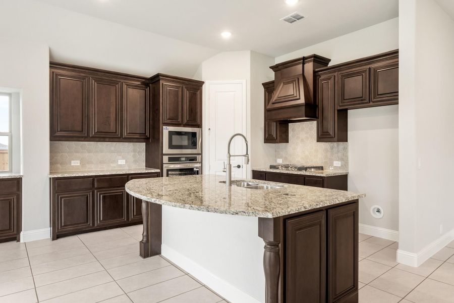Kitchen with dark wood cabinets, granite island with sink, stainless steel appliances, and tile backsplash Kitchen with dark wood cabinets, granite island with sink, stainless steel appliances, and tile backsplash