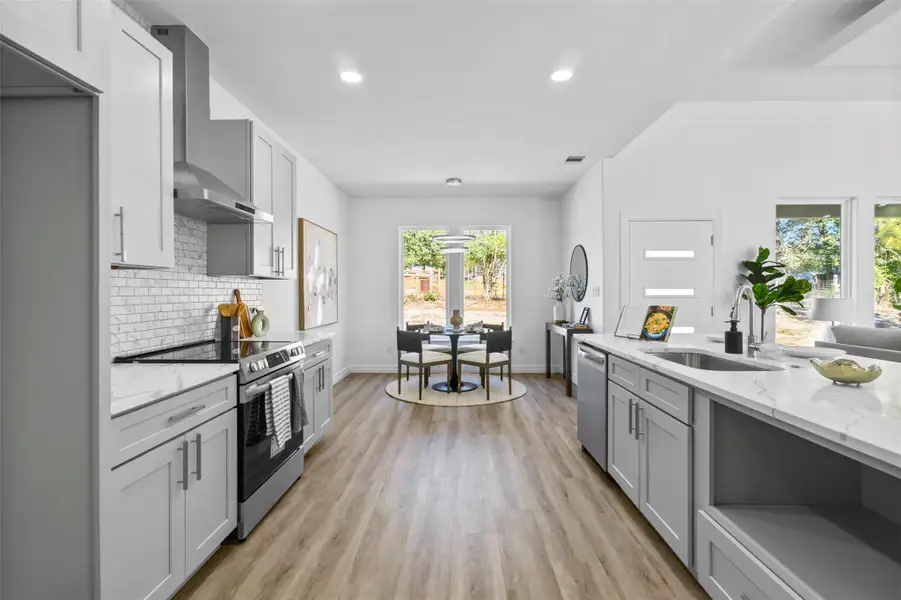 Kitchen featuring stainless steel appliances, light stone counters, decorative backsplash, wall chimney range hood, and light wood-style floors