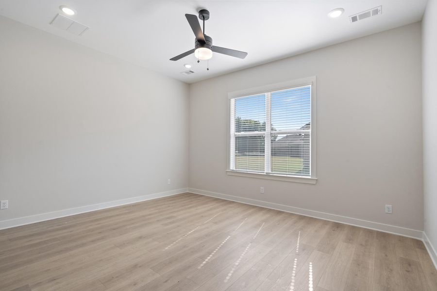 Spacious room featuring light wood-finish flooring, a ceiling fan with integrated lighting, recessed ceiling lights, and a large window with horizontal blinds Spacious room featuring light wood-finish flooring, a ceiling fan with integrated lighting, recessed ceiling lights, and a large window with horizontal blinds