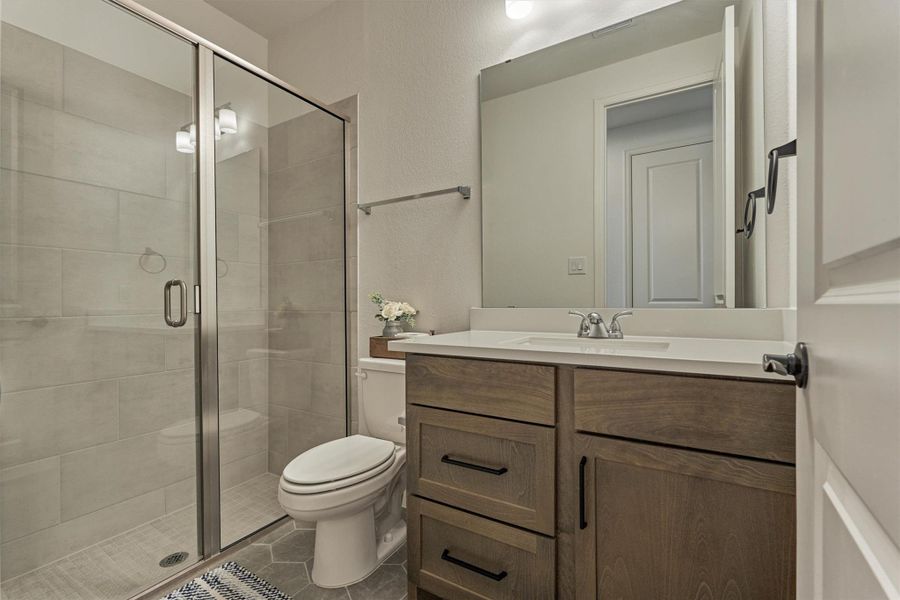 This sleek secondary bathroom combines modern elegance with functionality, featuring a spacious glass-enclosed shower, chic wood cabinetry, and stylish fixtures for a refreshing retreat.