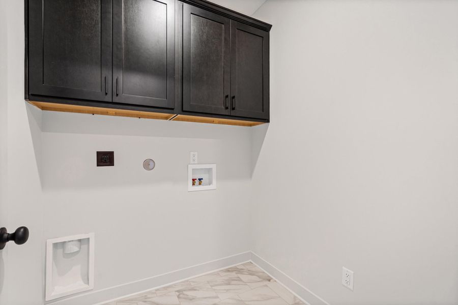 Laundry area featuring dark wood cabinetry, light-toned walls, and marble-look tile flooring Laundry area featuring dark wood cabinetry, light-toned walls, and marble-look tile flooring
