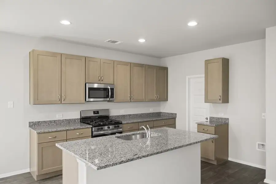 A kitchen with gray marble countertops, gray cabinets, vinyl flooring, a central island, and steel kitchen appliances.