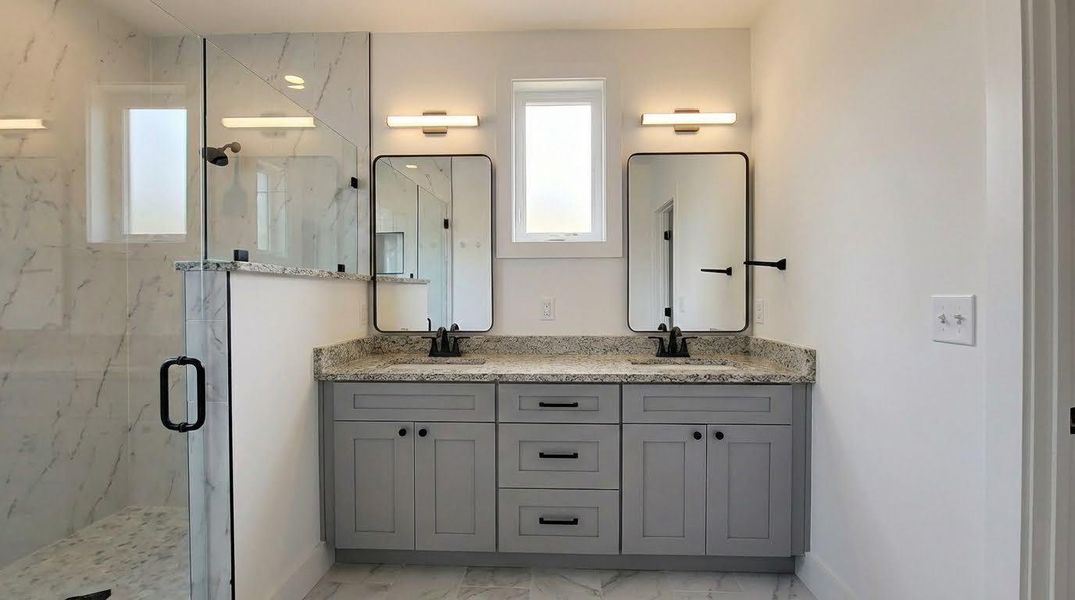 Bathroom featuring double vanity, a marble finish shower, and light marble finish flooring