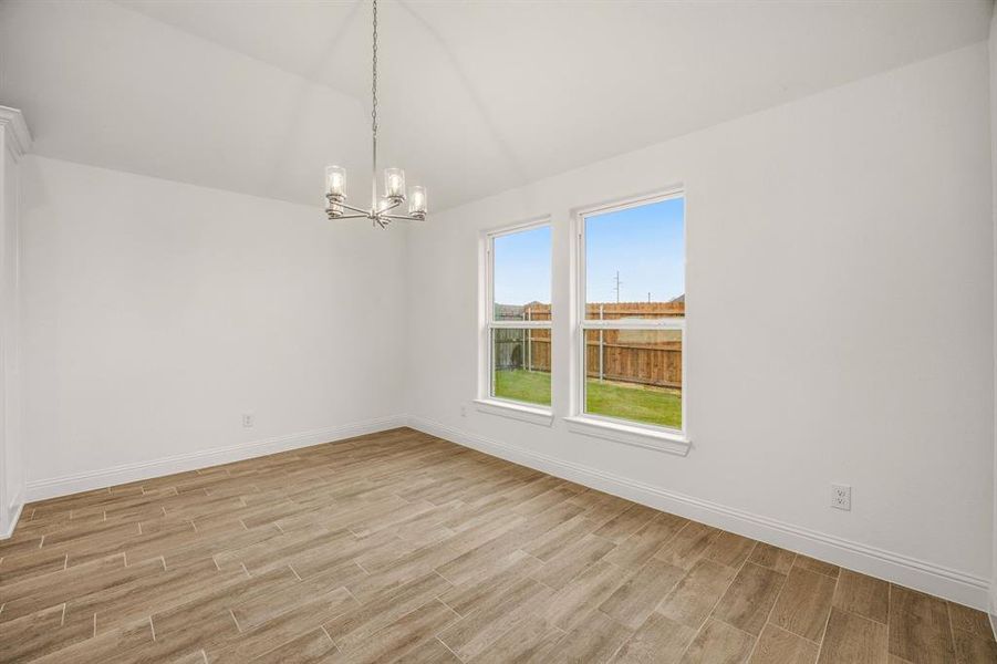 This bright room features a vaulted ceiling with a modern chandelier, two large windows providing views of the fenced yard, and wood-look tile flooring