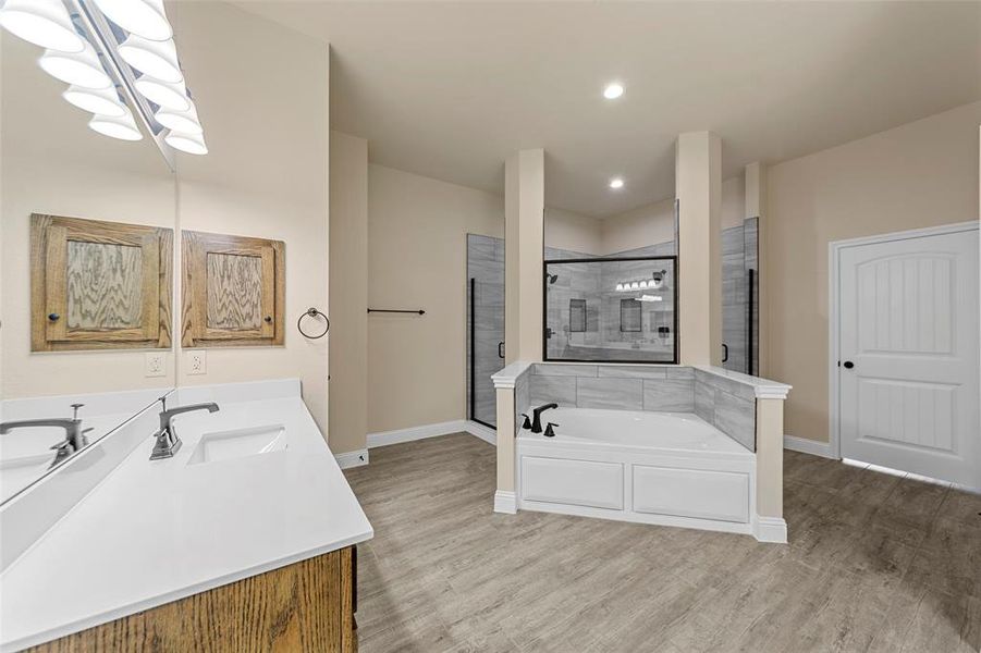 Full bath featuring a stall shower, baseboards, wood finished floors, a bath, and recessed lighting