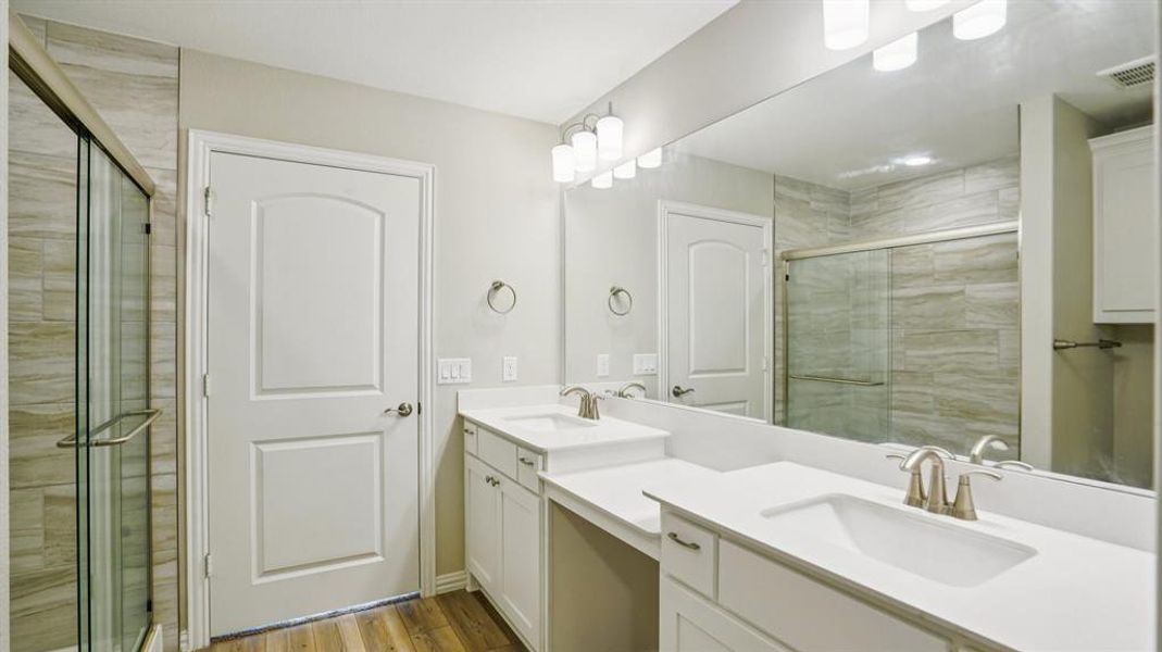 Full bathroom featuring double vanity, light wood-style floors, and a stall shower Full bathroom featuring double vanity, light wood-style floors, and a stall shower