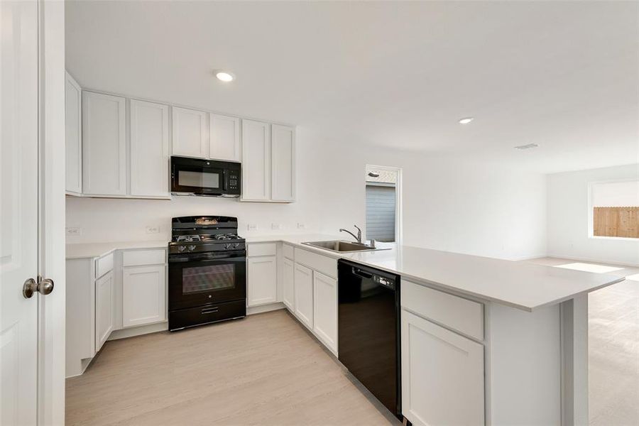 Kitchen with black appliances, white cabinets, a peninsula, recessed lighting, and light wood-type flooring Kitchen with black appliances, white cabinets, a peninsula, recessed lighting, and light wood-type flooring