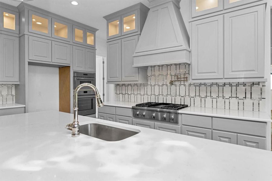 Crafted for the culinary enthusiast, this kitchen showcases a premium gas cooktop with pot filler, quartz counters, stainless steel oven and microwave, and soft-lit display cabinetry for a sleek, functional finish.