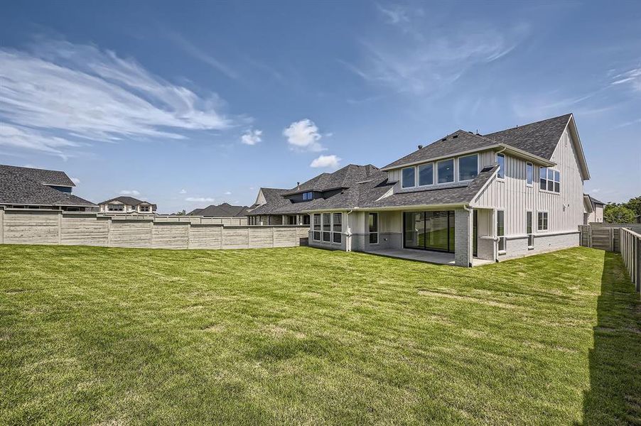 Rear view of house with board and batten siding, a shingled roof, a patio, and brick siding Rear view of house with board and batten siding, a shingled roof, a patio, and brick siding