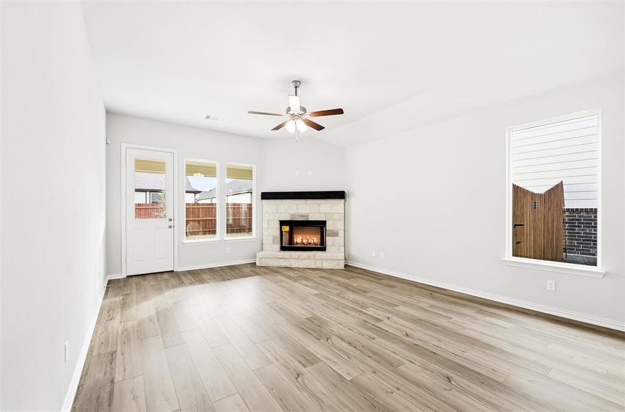 Unfurnished living room with a stone fireplace, light wood-type flooring, and a ceiling fan