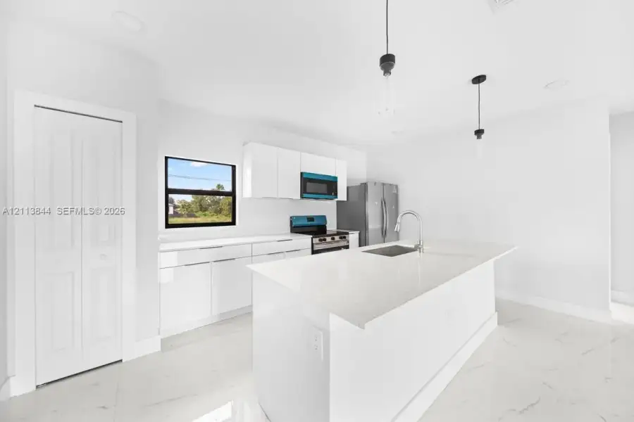 Kitchen featuring a center island with a stone-surface countertop, high-gloss white cabinetry, recessed ceiling lighting, pendant light fixtures, and white tile flooring Kitchen featuring a center island with a stone-surface countertop, high-gloss white cabinetry, recessed ceiling lighting, pendant light fixtures, and white tile flooring
