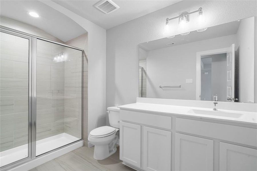 Secondary bath features stained wood cabinets, beautiful countertops, mirror, tile flooring, and large walk-in shower with tile surround.