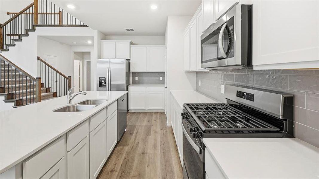 Modern kitchen featuring an island with an undermount dual-basin sink, white shaker cabinetry, stainless steel appliances, a gas range, and wood-finish flooring