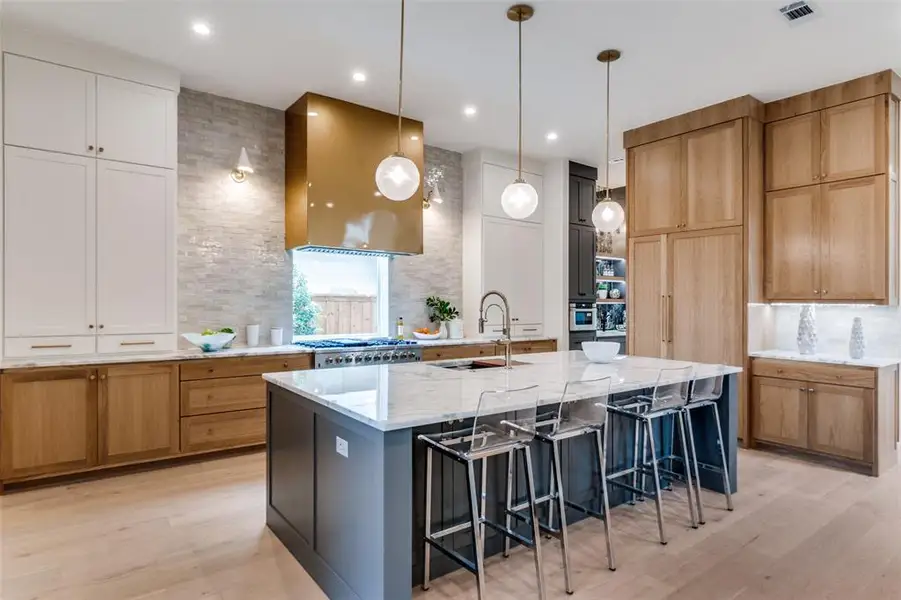 Kitchen with a sink, visible vents, light wood-style flooring, range hood, and light stone countertops Kitchen with a sink, visible vents, light wood-style flooring, range hood, and light stone countertops