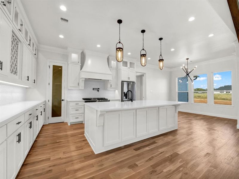 Kitchen featuring custom exhaust hood, light hardwood / wood-style floors, a large island with sink, and appliances with stainless steel finishes