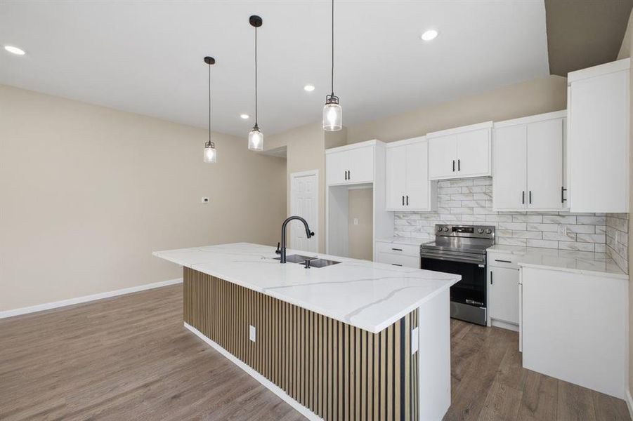 Kitchen featuring stainless steel electric range oven, a kitchen island with sink, light stone countertops, white cabinetry, and pendant lighting Kitchen featuring stainless steel electric range oven, a kitchen island with sink, light stone countertops, white cabinetry, and pendant lighting