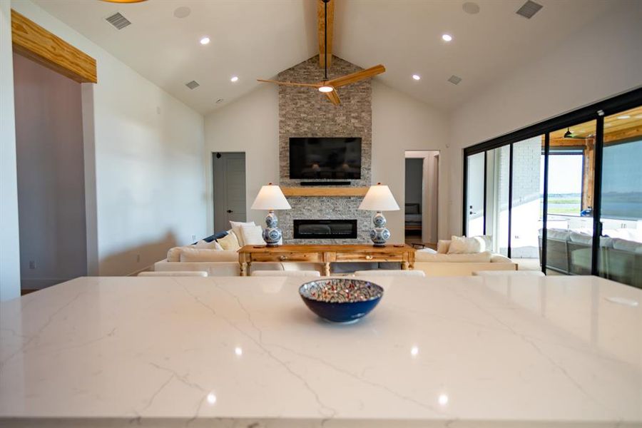 Kitchen featuring beam ceiling, light stone counters, a fireplace, open floor plan, and high vaulted ceiling Kitchen featuring beam ceiling, light stone counters, a fireplace, open floor plan, and high vaulted ceiling