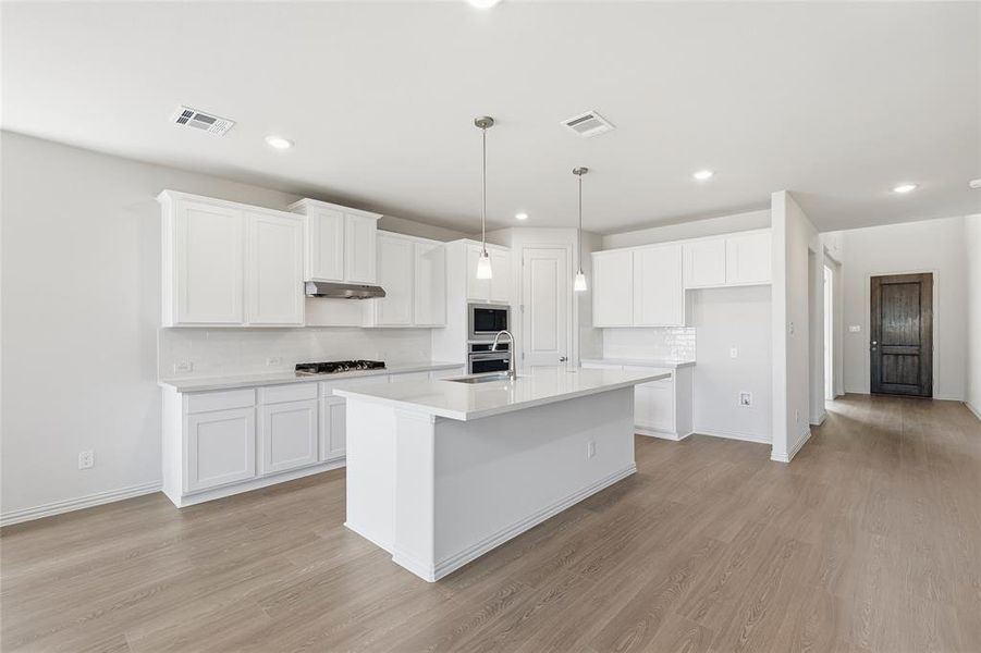 Kitchen with backsplash, white cabinetry, hanging light fixtures, light wood finished floors, and recessed lighting Kitchen with backsplash, white cabinetry, hanging light fixtures, light wood finished floors, and recessed lighting
