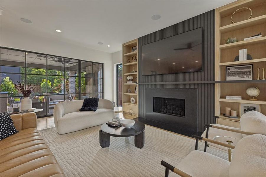 Living area featuring a modern black fireplace with a slatted accent wall, surrounded by built-in wood shelving Living area featuring a modern black fireplace with a slatted accent wall, surrounded by built-in wood shelving