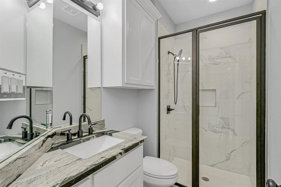 Bathroom with a marble finish shower, toilet, and vanity