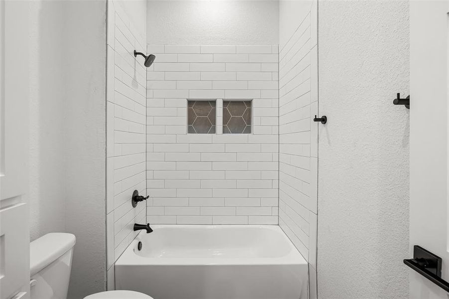 Bathroom featuring tiled shower / bath combo and toilet