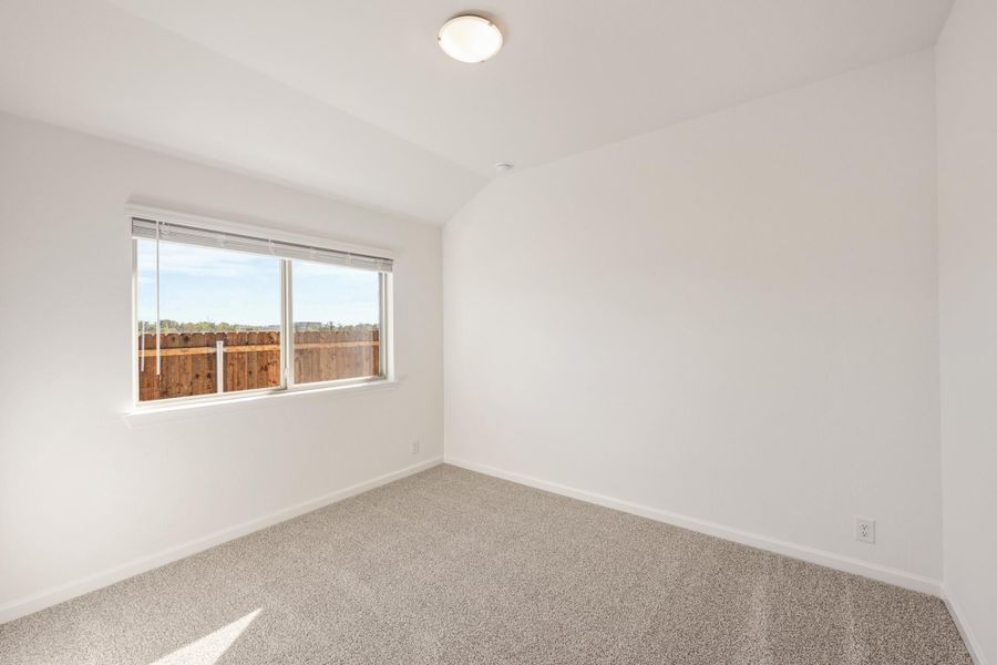 Empty bedroom with white walls, gray carpet, and a window overlooking a wood fence