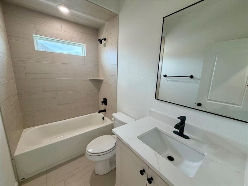 Bathroom featuring a bathtub with subway tile surround, matte black fixtures, an elongated window, a modern vanity with integrated sink, and a framed mirror