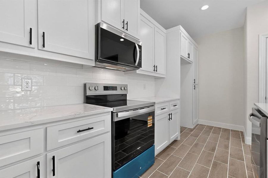 Kitchen with stainless steel appliances, backsplash, white cabinets, light stone countertops, and recessed lighting Kitchen with stainless steel appliances, backsplash, white cabinets, light stone countertops, and recessed lighting