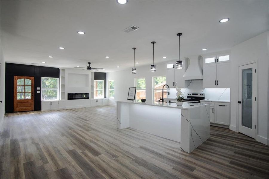 Kitchen featuring dark hardwood / wood-style flooring, custom range hood, a kitchen island with sink, white cabinets, and stainless steel range with electric cooktop