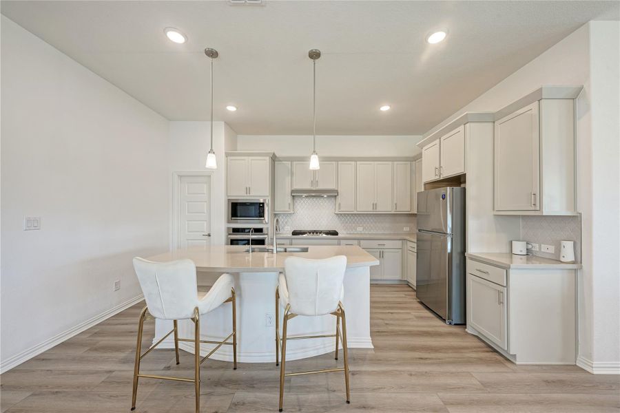 A contemporary kitchen features a spacious island with bar seating, integrated appliances, and sleek pendant lighting.