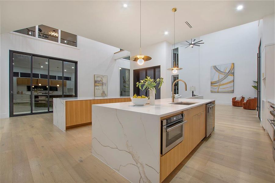 Kitchen with pendant lighting, a large island with sink, sink, appliances with stainless steel finishes, and light hardwood / wood-style floors