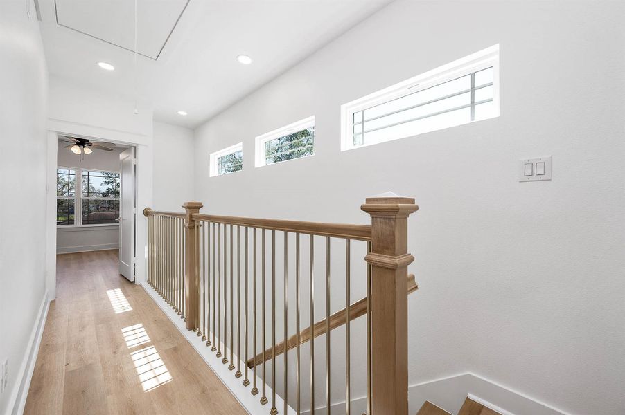 Upstairs hallway featuring natural light, wood railing details, and a bright open feel.
