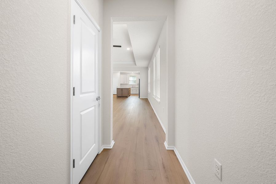 A well-lit corridor with rich wood flooring leads the eye to a modern kitchen. A well-lit corridor with rich wood flooring leads the eye to a modern kitchen.