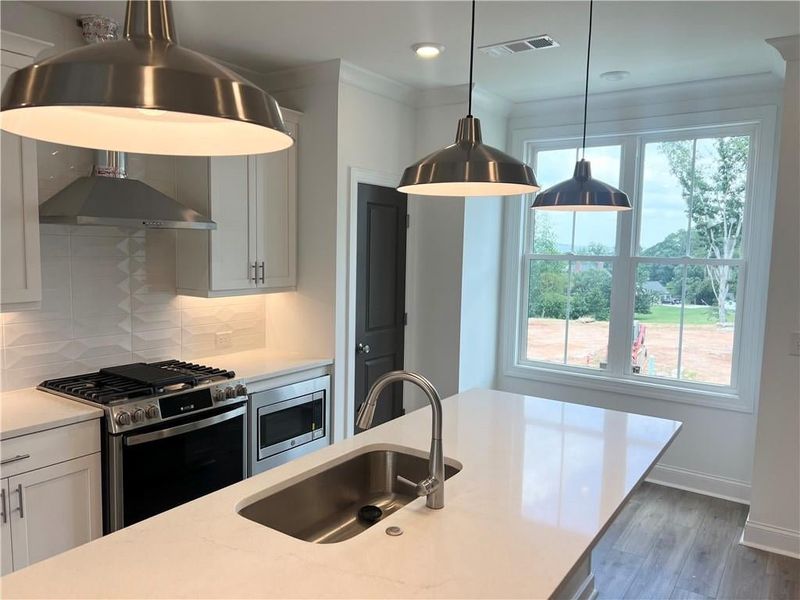 Kitchen with appliances with stainless steel finishes, wall chimney exhaust hood, decorative backsplash, light countertops, and wood finished floors
