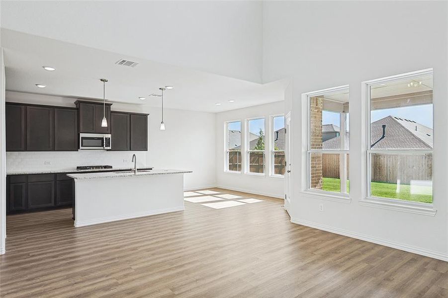 Kitchen featuring a kitchen island with sink, open floor plan, hanging light fixtures, light stone countertops, and dark brown cabinets Kitchen featuring a kitchen island with sink, open floor plan, hanging light fixtures, light stone countertops, and dark brown cabinets