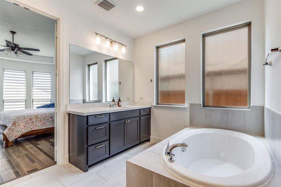 Ensuite bathroom with vanity, a bath, light tile patterned floors, and recessed lighting