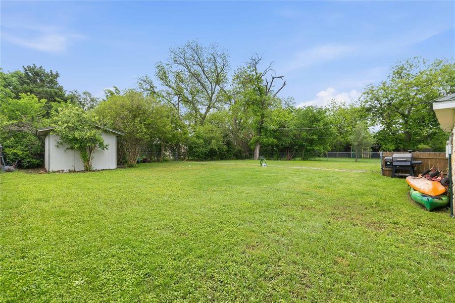 Expansive grassy backyard featuring a white storage shed and perimeter fencing Expansive grassy backyard featuring a white storage shed and perimeter fencing