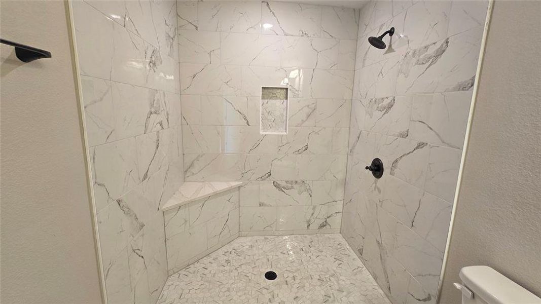 Bathroom featuring tiled shower and a textured wall