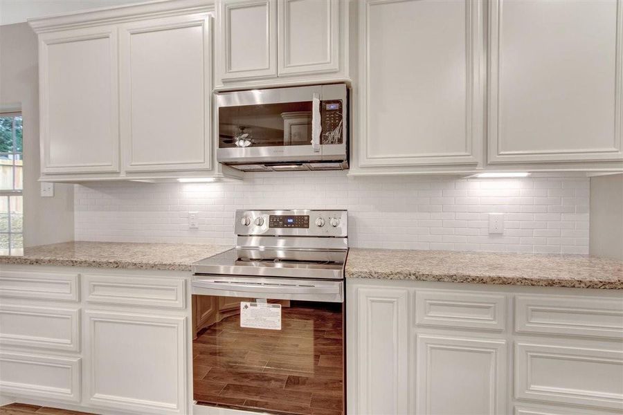 Modern kitchen featuring stainless steel appliances, white cabinetry, and a sample tile backsplash. Sample Modern kitchen featuring stainless steel appliances, white cabinetry, and a sample tile backsplash. Sample