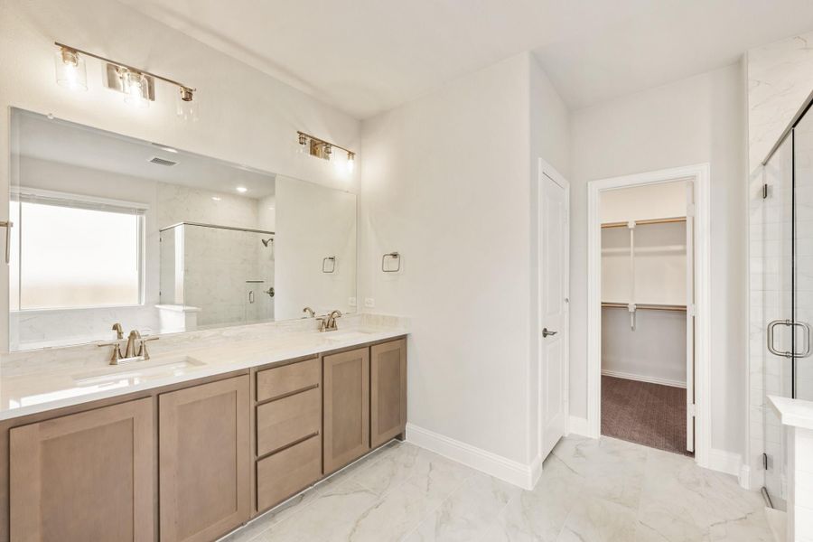 Master bathroom with double vanity, wood cabinets, glass shower, and walk-in closet entrance Master bathroom with double vanity, wood cabinets, glass shower, and walk-in closet entrance