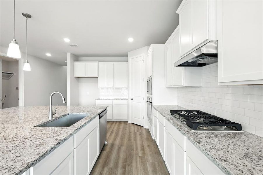 Kitchen with under cabinet range hood, stainless steel appliances, light wood-style floors, white cabinets, and backsplash Kitchen with under cabinet range hood, stainless steel appliances, light wood-style floors, white cabinets, and backsplash