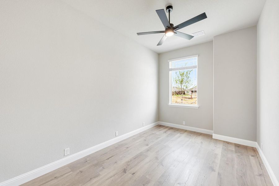 Empty bedroom with light hardwood floors, ceiling fan, and single window with backyard view