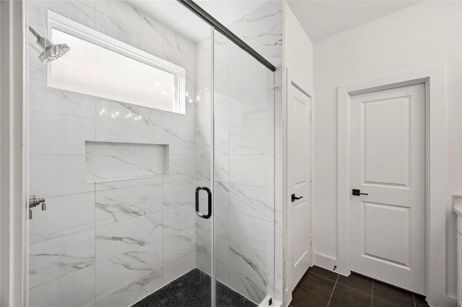 The spacious walk-in shower is beautifully finished with a hexagonal tile floor, floor-to-ceiling tile surround, and an obscure-glass window that welcomes natural light while maintaining privacy. The door to the right is the primary closet complete with a built-in safe. The spacious walk-in shower is beautifully finished with a hexagonal tile floor, floor-to-ceiling tile surround, and an obscure-glass window that welcomes natural light while maintaining privacy. The door to the right is the primary closet complete with a built-in safe.