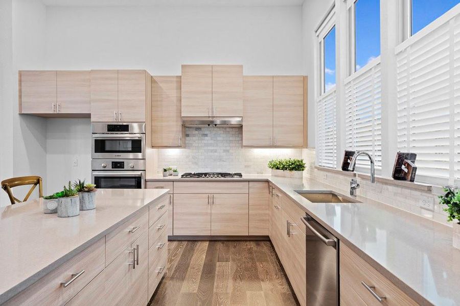 Kitchen featuring light brown cabinets, backsplash, light stone counters, dark wood-type flooring, and stainless steel appliances