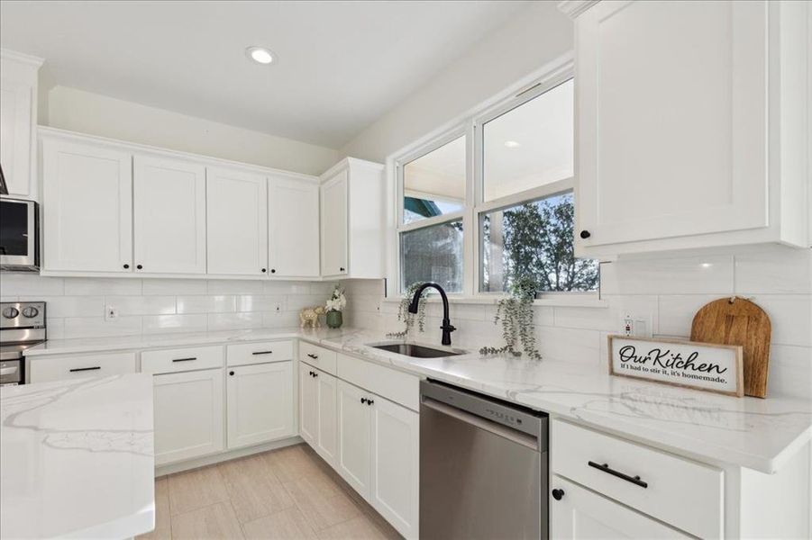 Kitchen featuring appliances with stainless steel finishes, sink, white cabinets, and decorative backsplash