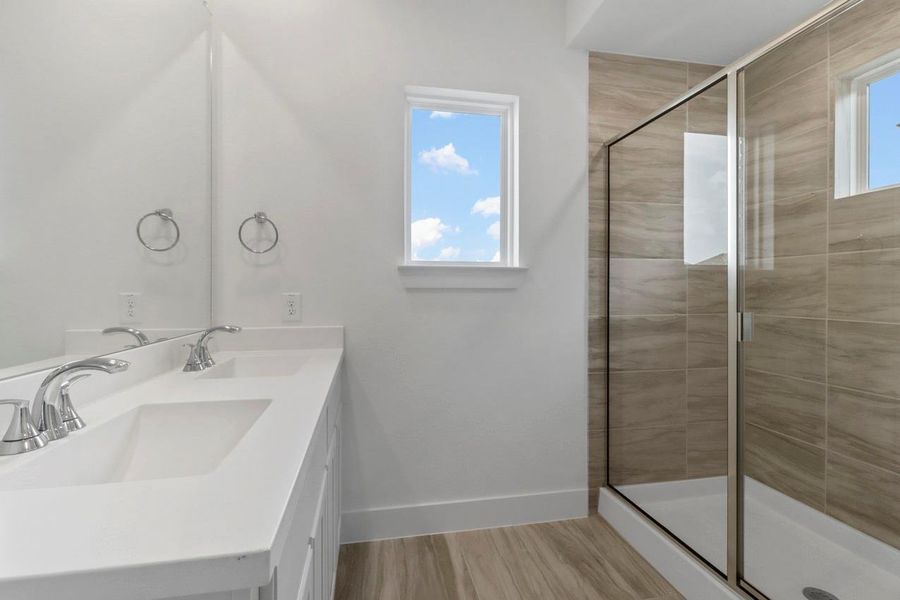 A stylish primary bathroom featuring ample cabinets, bright lighting, a spacious shower, and a window that fills the space with natural light. A stylish primary bathroom featuring ample cabinets, bright lighting, a spacious shower, and a window that fills the space with natural light.