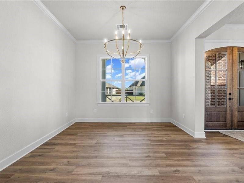 Unfurnished dining area featuring a chandelier, wood finished floors, and ornamental molding